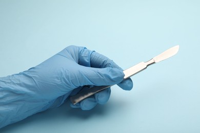 Photo of Doctor with surgical scalpel on light blue background, closeup