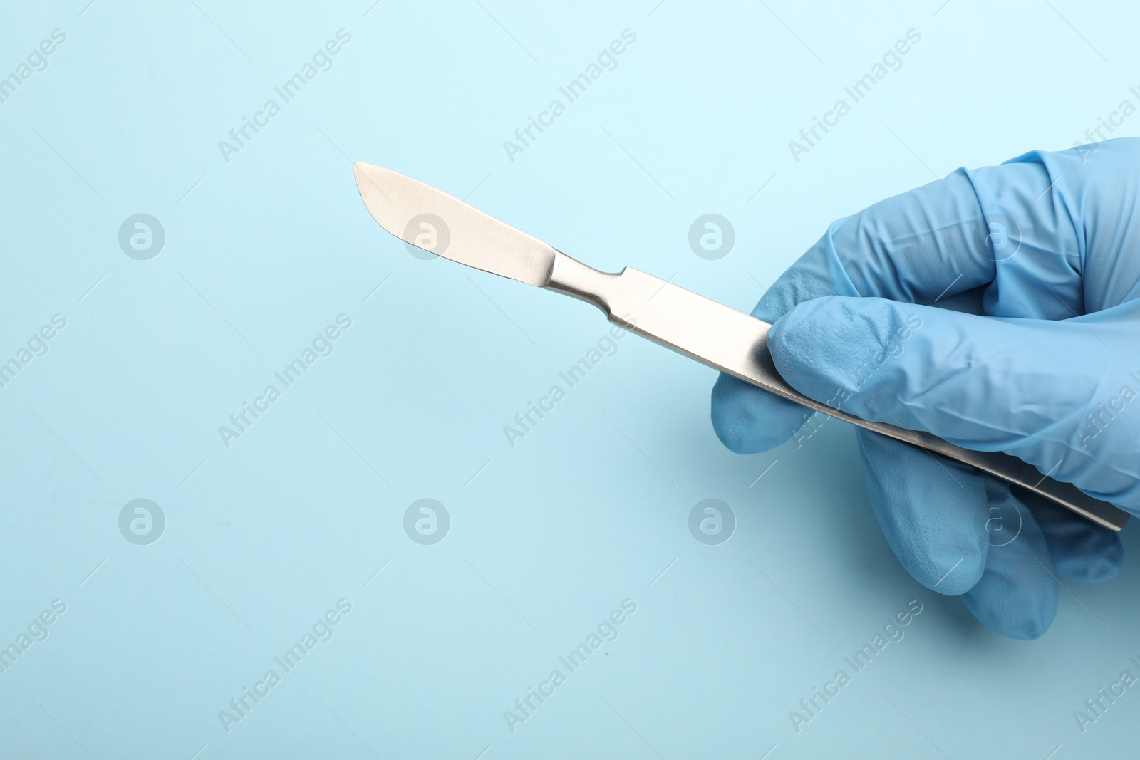 Photo of Doctor with surgical scalpel on light blue background, closeup. Space for text