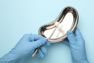 Photo of Doctor holding surgical tweezers with gauze and tray on light blue background, top view