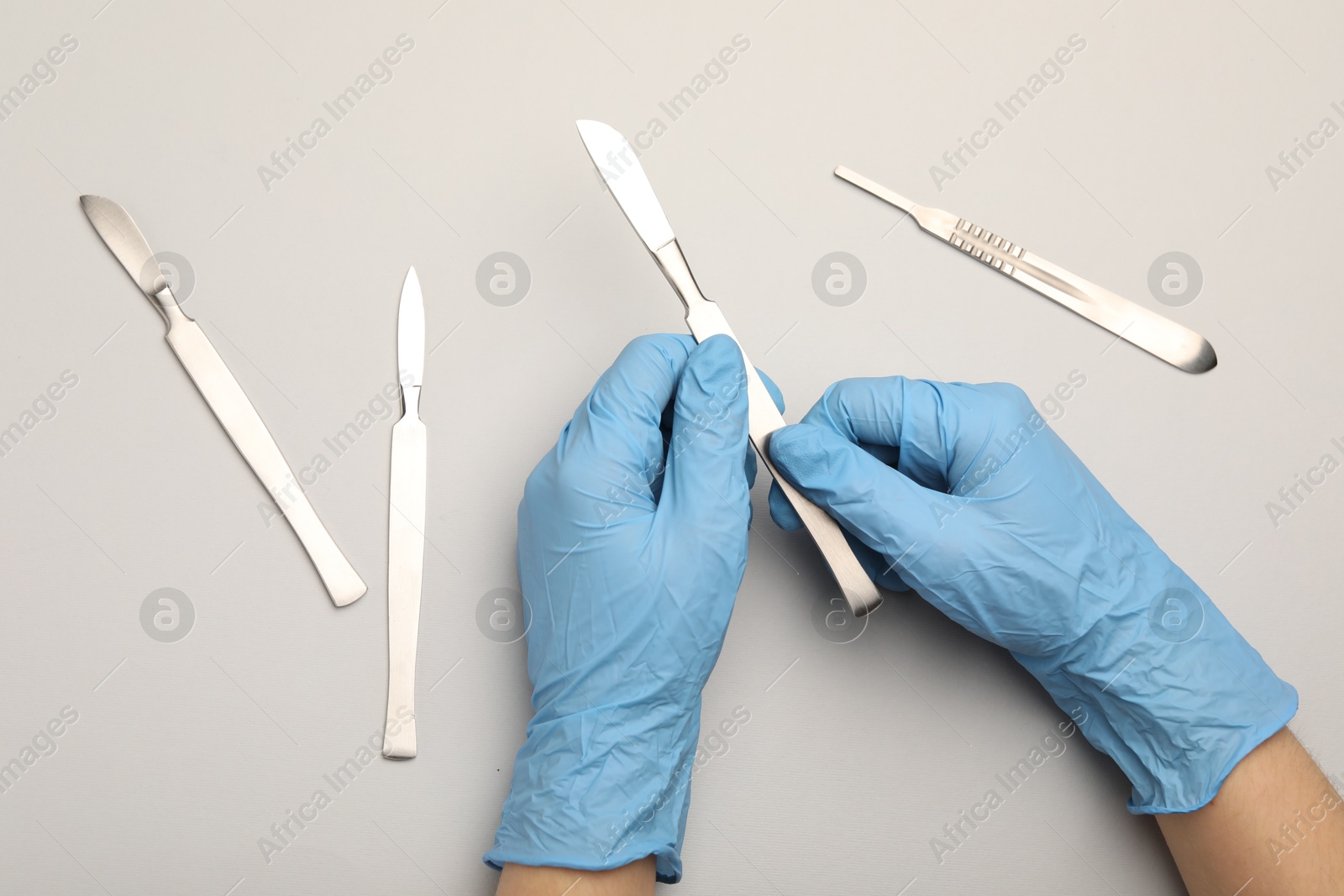 Photo of Doctor with surgical scalpels on light background, top view