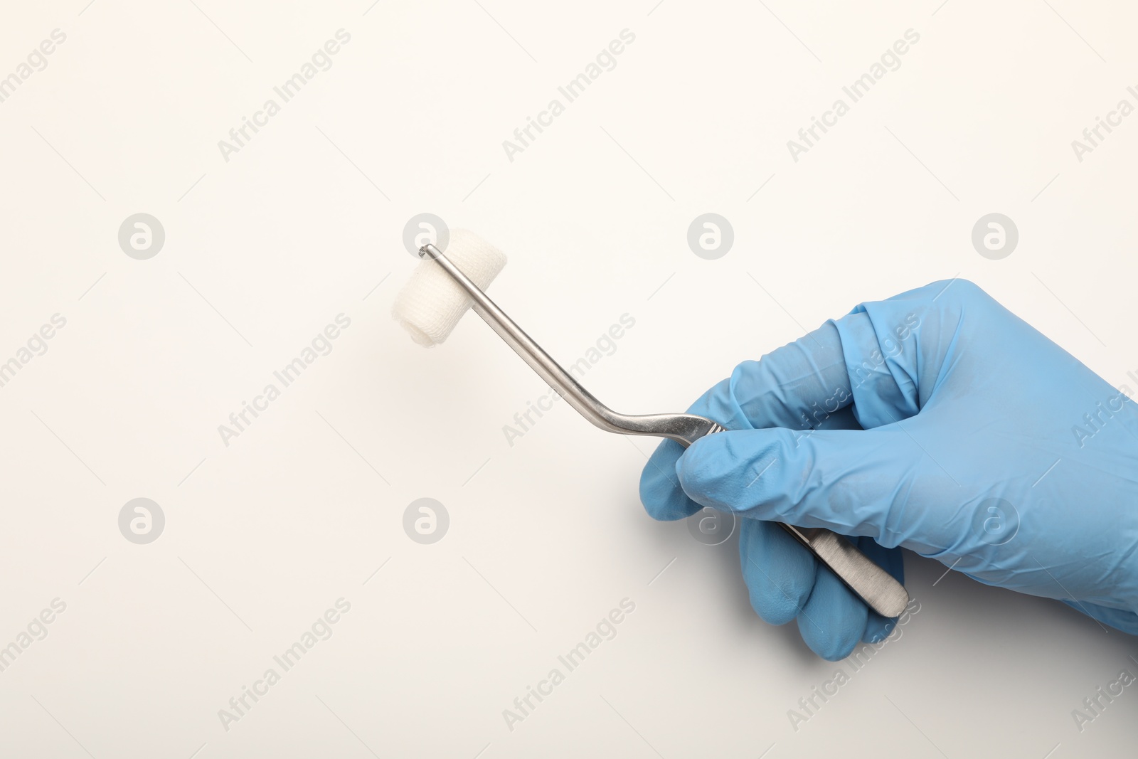 Photo of Doctor holding surgical tweezers with gauze on light background, top view. Space for text