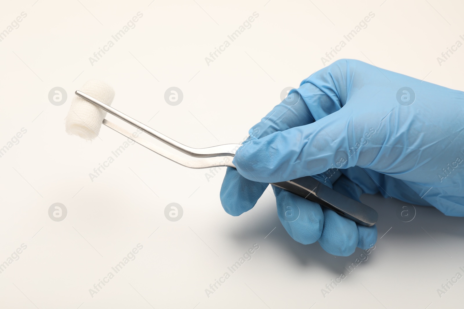 Photo of Doctor holding surgical tweezers with gauze on light background, closeup