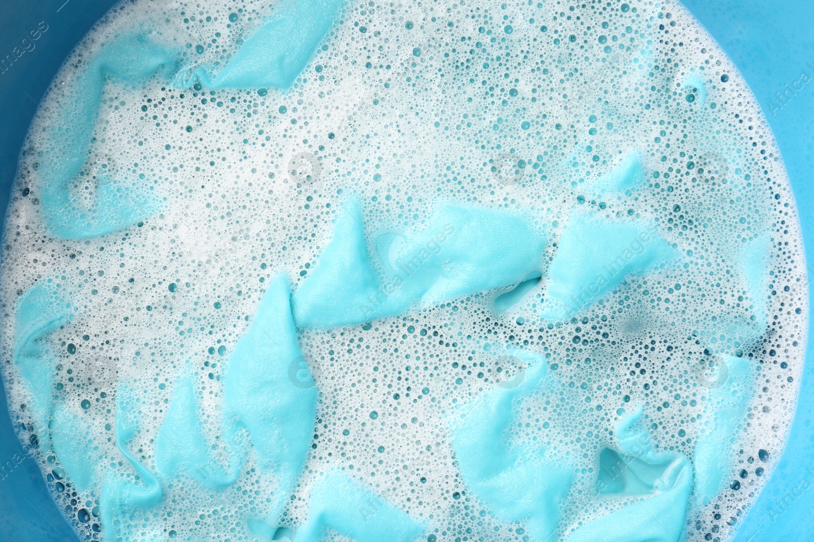 Photo of Turquoise clothes soaked in water before washing, top view