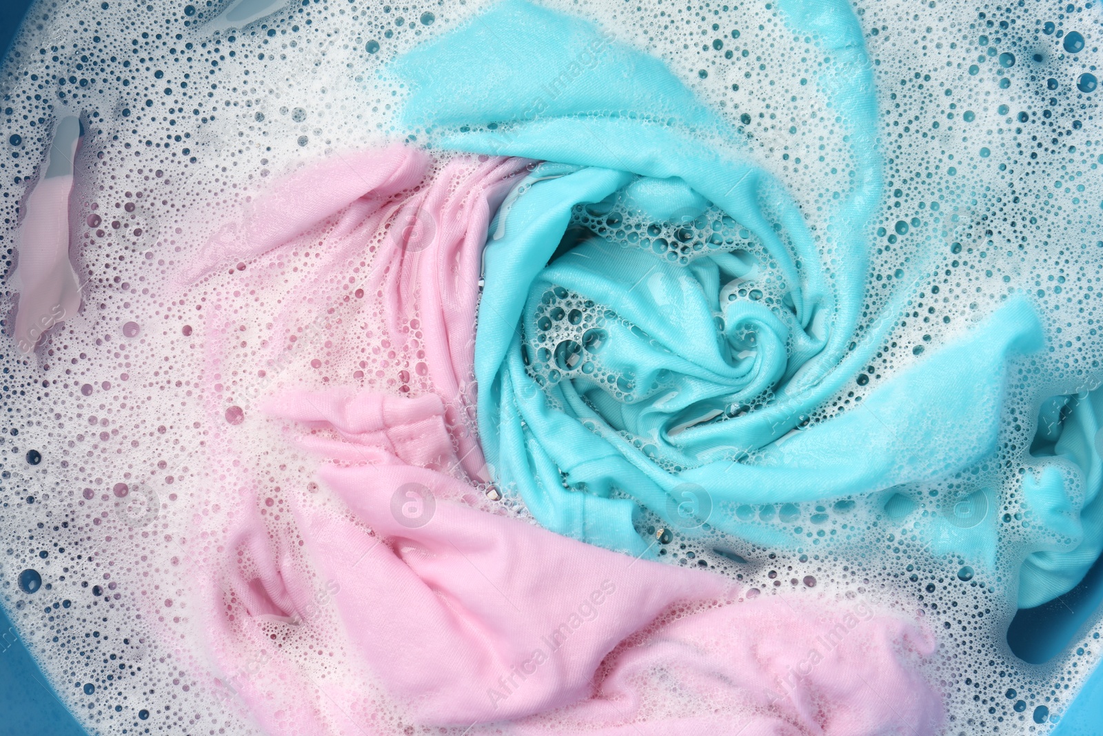 Photo of Colorful clothes soaked in water before washing, top view