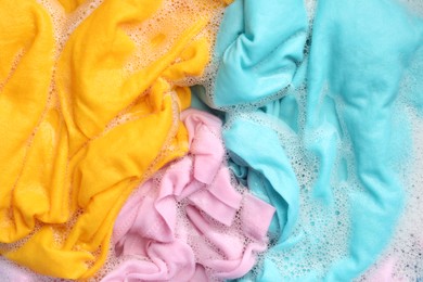 Photo of Colorful clothes soaked in water before washing, top view