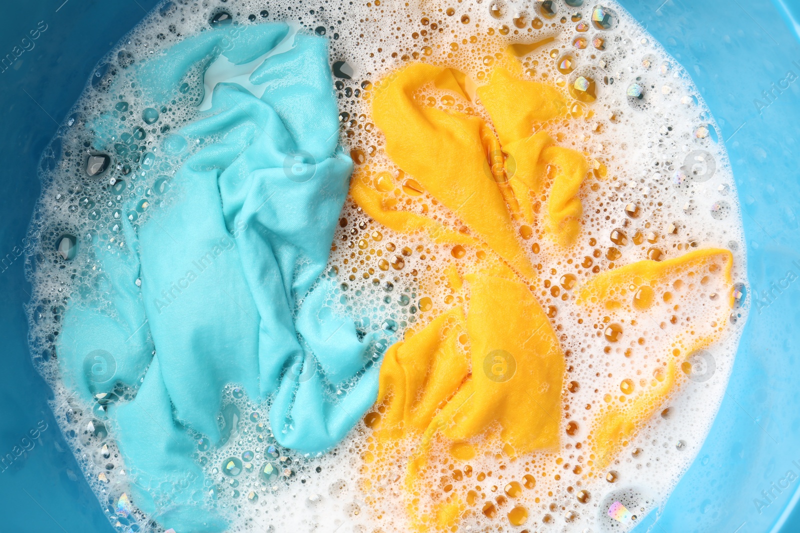 Photo of Colorful clothes soaked in water before washing, top view