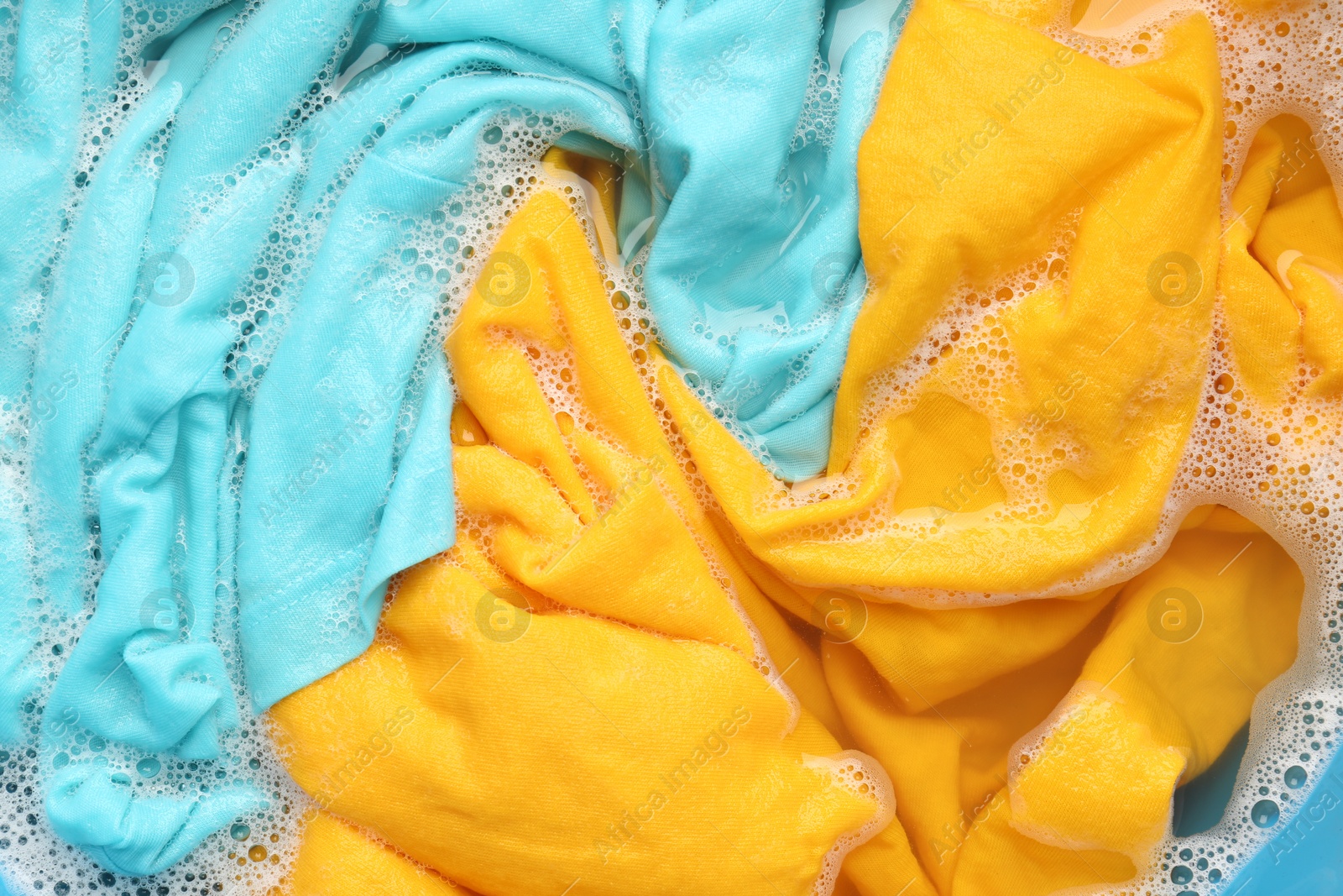 Photo of Colorful clothes soaked in water before washing, top view