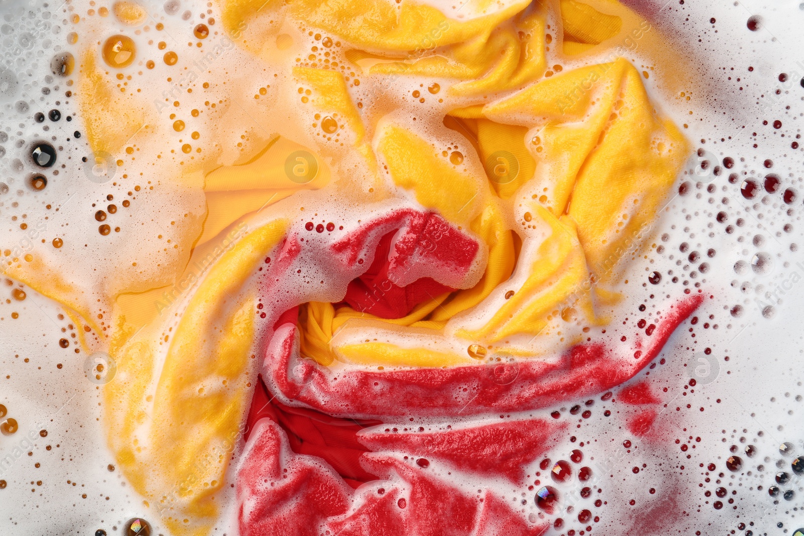 Photo of Colorful clothes soaked in water before washing, top view