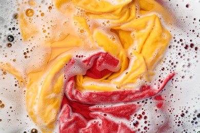 Photo of Colorful clothes soaked in water before washing, top view