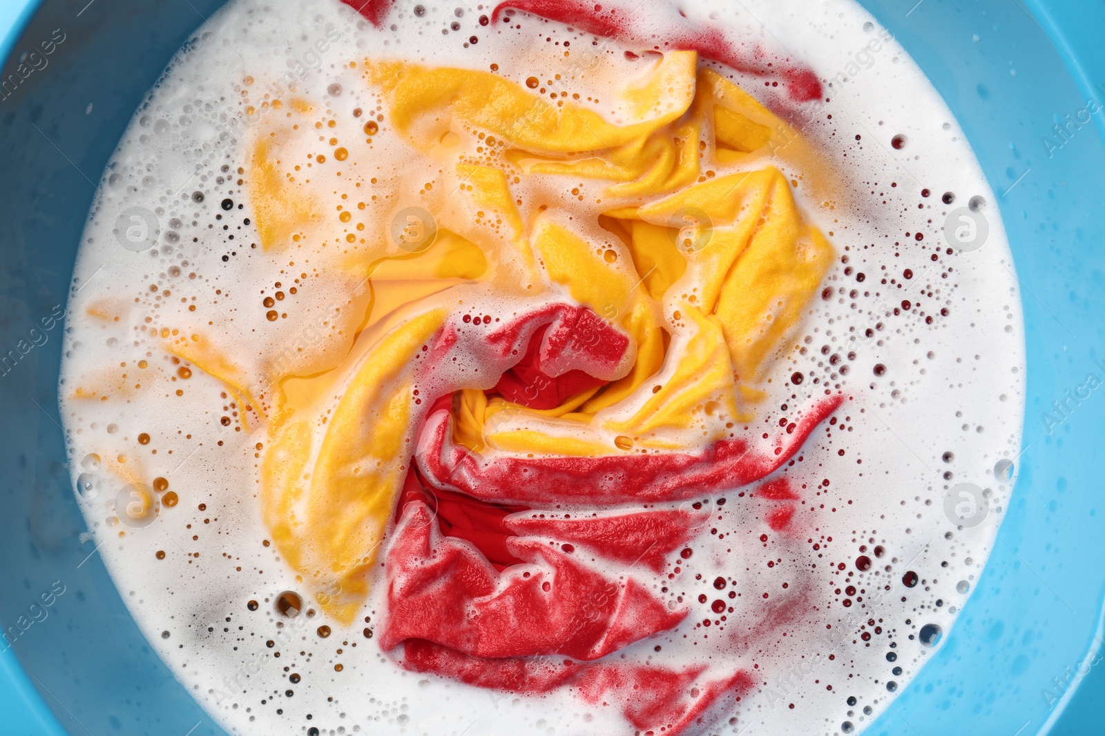 Photo of Colorful clothes soaked in water before washing, top view