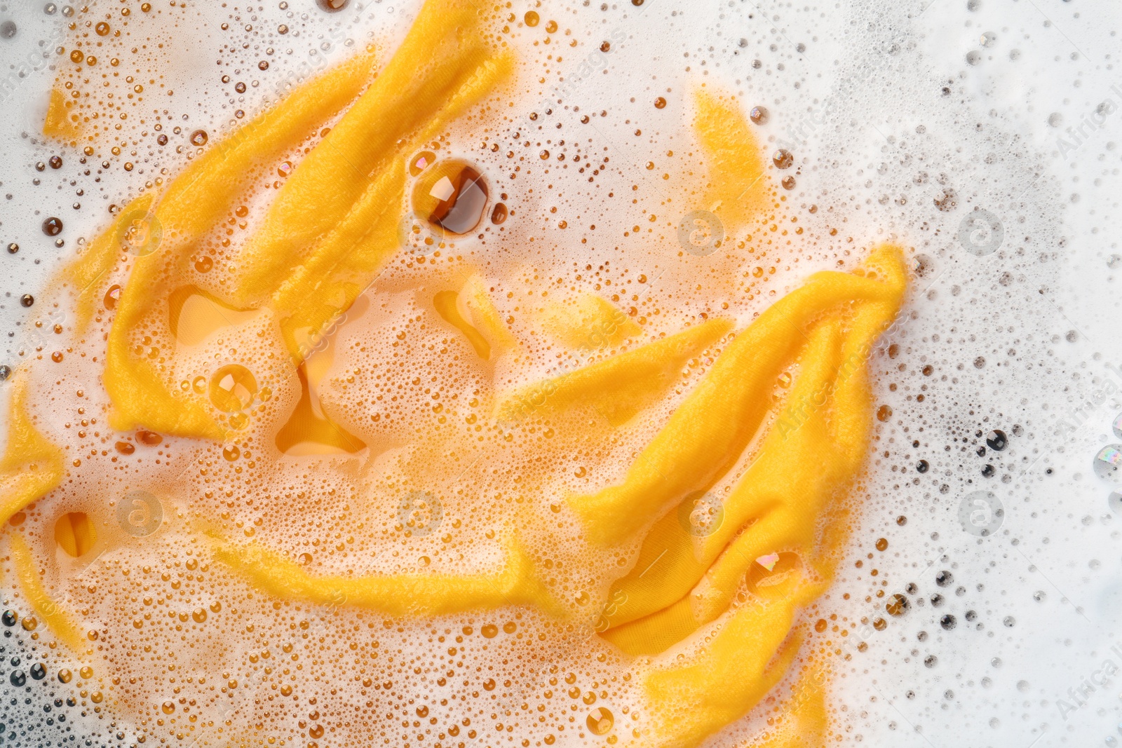 Photo of Yellow clothes soaked in water before washing, top view