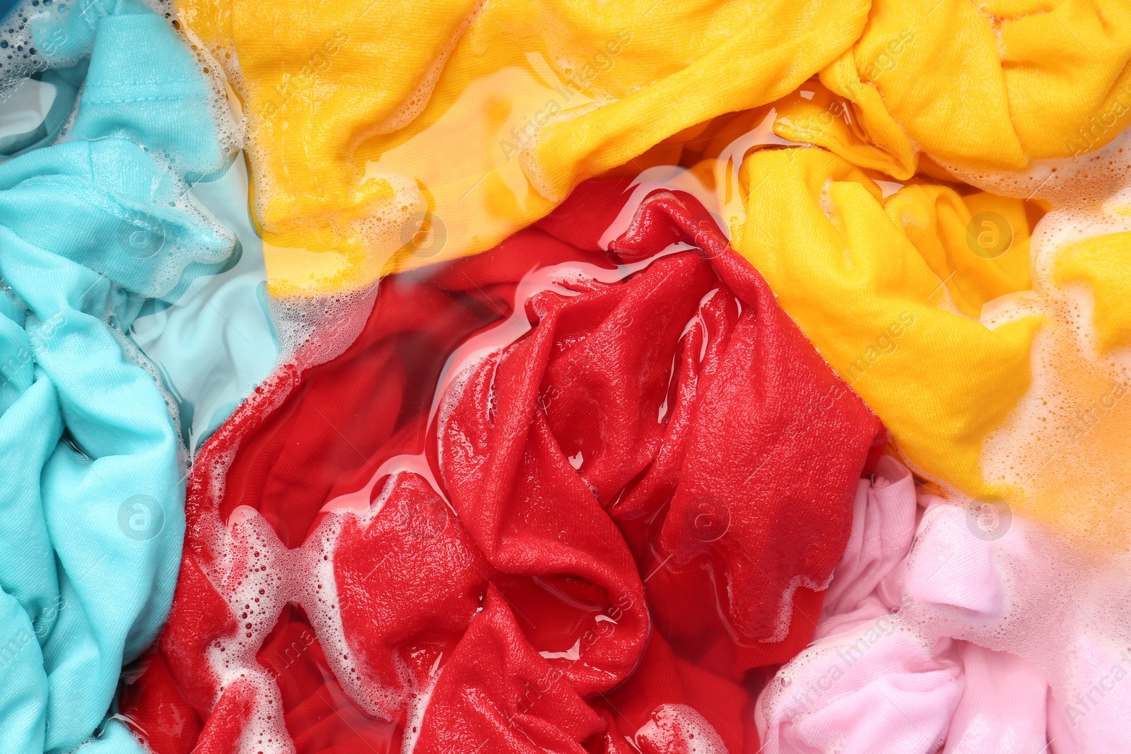 Photo of Colorful clothes soaked in water before washing, top view