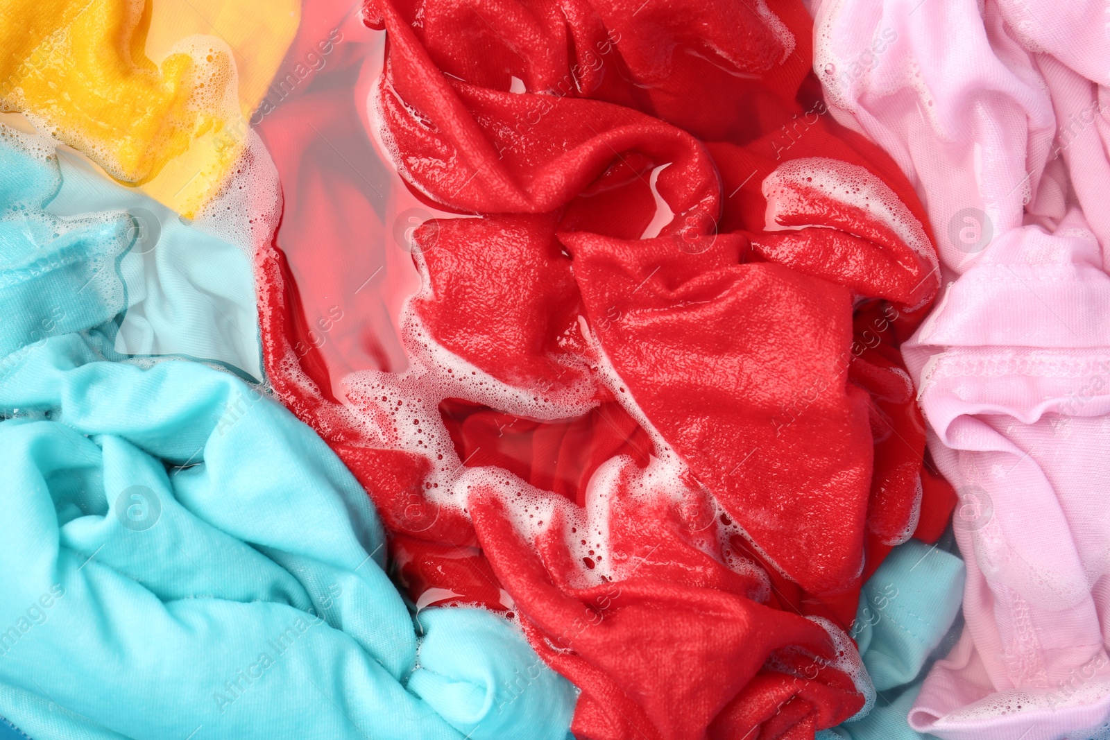 Photo of Colorful clothes soaked in water before washing, top view