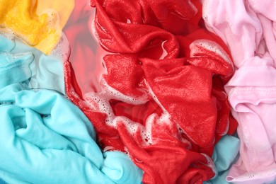 Photo of Colorful clothes soaked in water before washing, top view