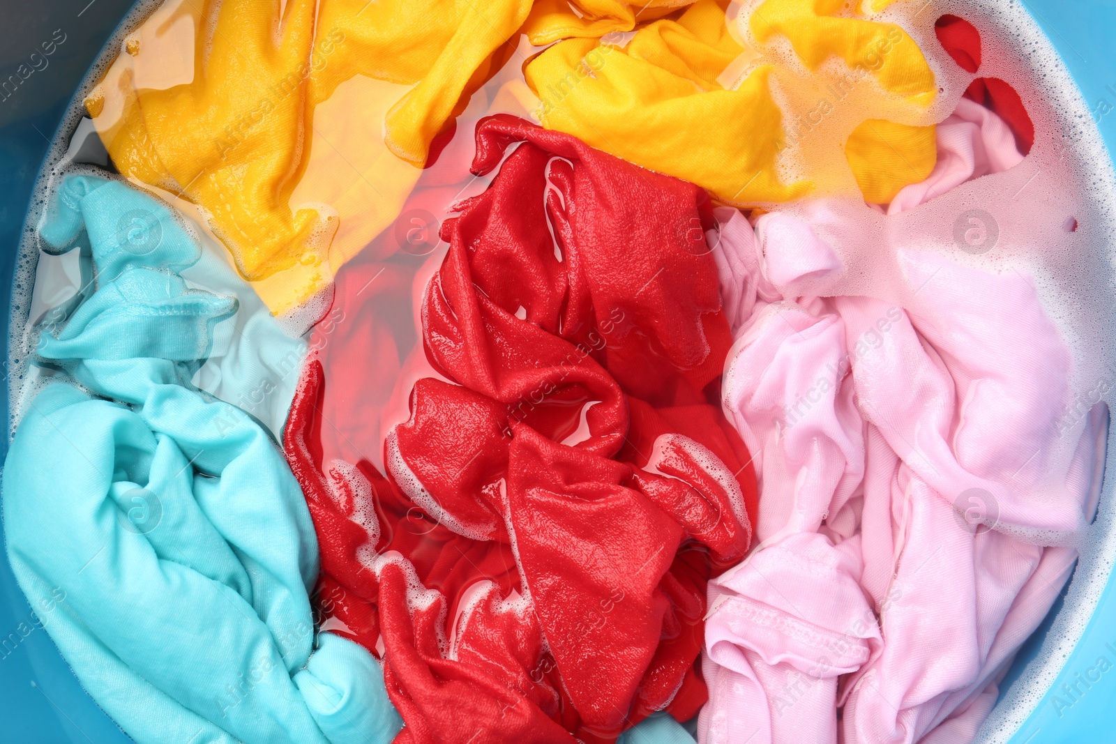 Photo of Colorful clothes soaked in water before washing, top view