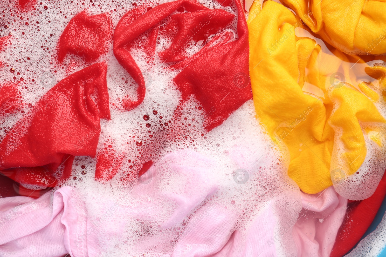 Photo of Colorful clothes soaked in water before washing, top view