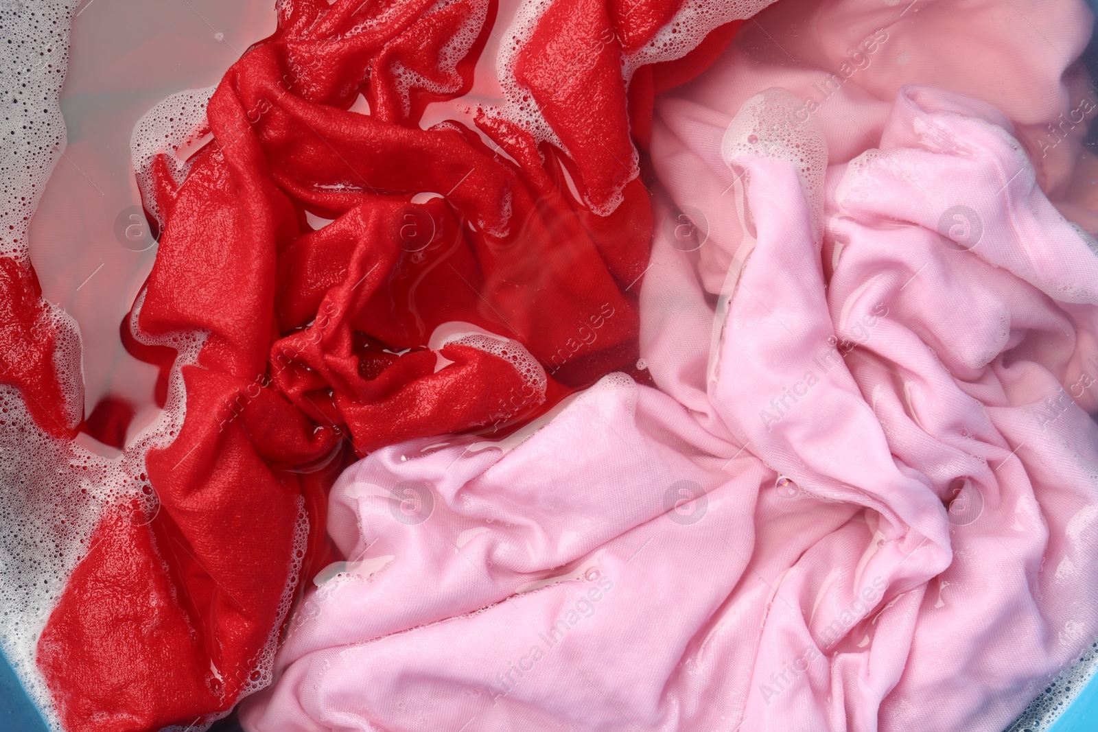 Photo of Colorful clothes soaked in water before washing, top view