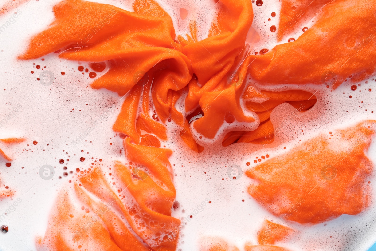 Photo of Orange clothes soaked in water before washing, top view