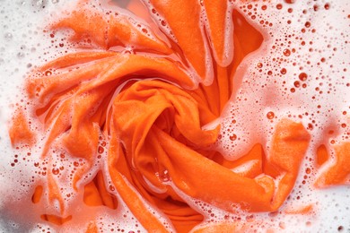 Photo of Orange clothes soaked in water before washing, top view