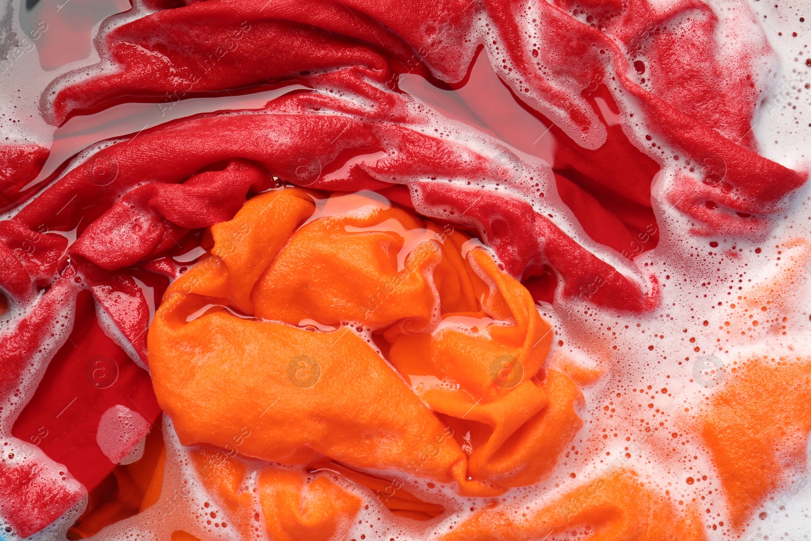 Photo of Colorful clothes soaked in water before washing, top view