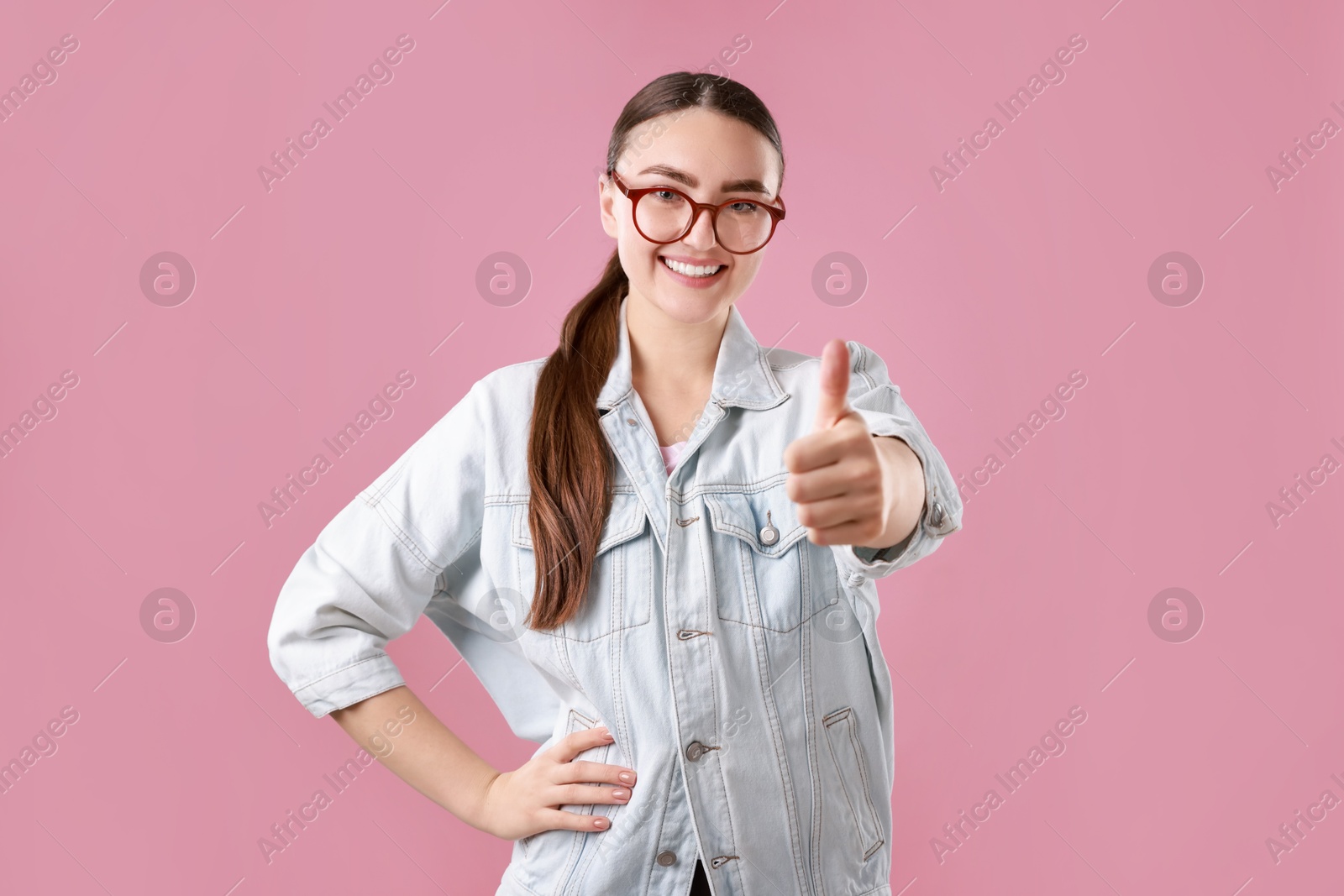 Photo of Happy woman showing thumbs up on pink background. Like gesture