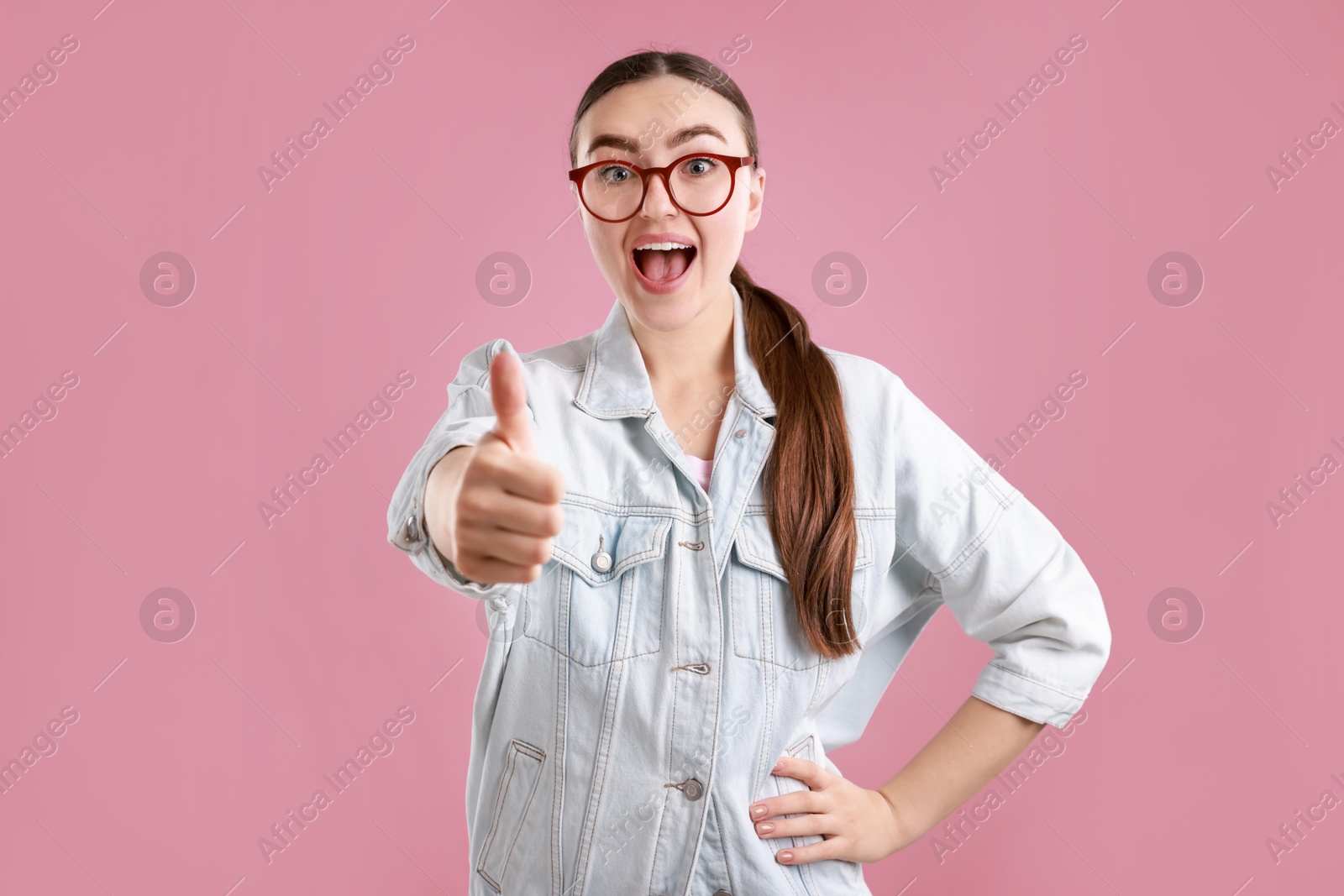 Photo of Emotional woman showing thumbs up on pink background. Like gesture