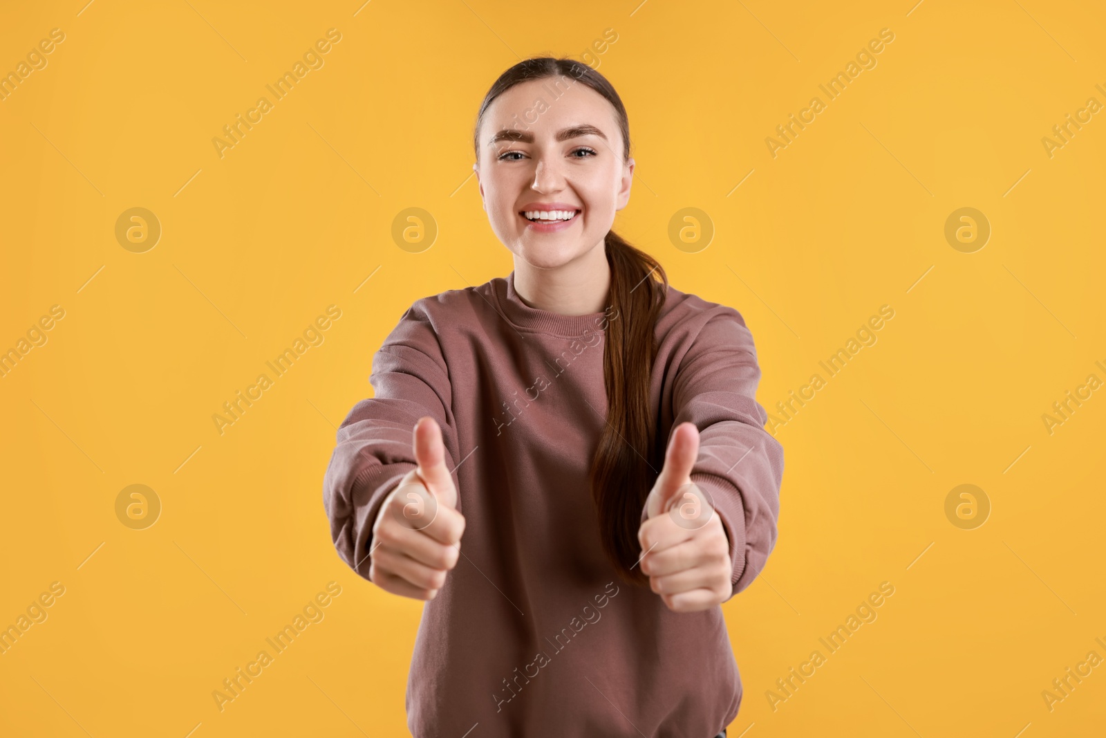 Photo of Happy woman showing thumbs up on yellow background. Like gesture