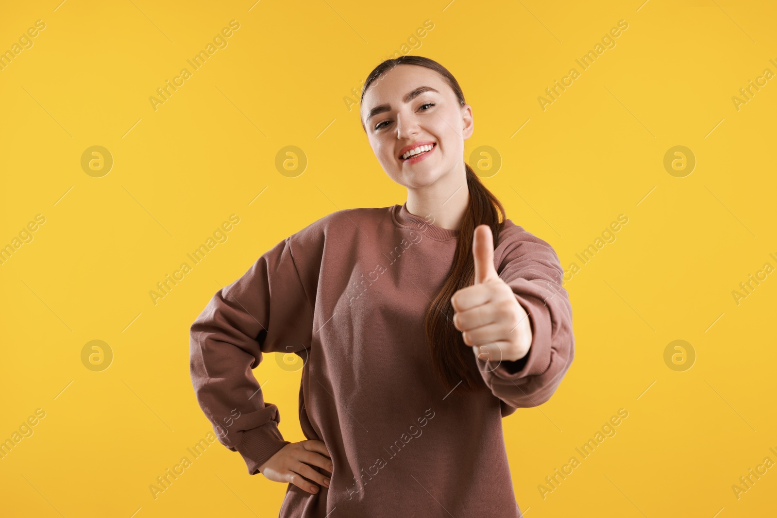 Photo of Happy woman showing thumbs up on yellow background. Like gesture