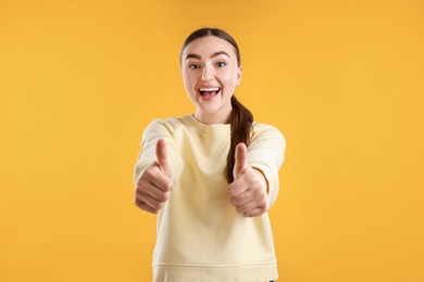 Happy woman showing thumbs up on yellow background. Like gesture