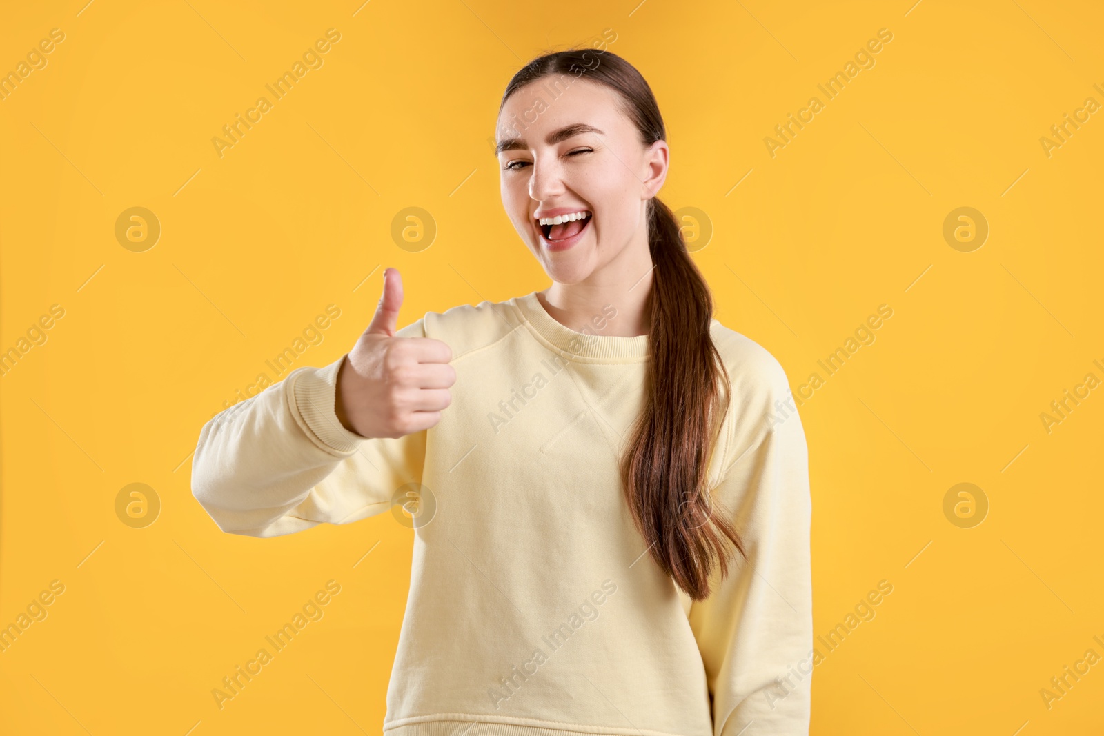 Photo of Happy woman showing thumbs up on yellow background. Like gesture