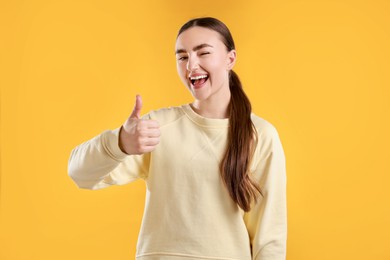 Photo of Happy woman showing thumbs up on yellow background. Like gesture