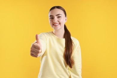 Happy woman showing thumbs up on yellow background. Like gesture