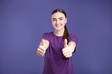 Photo of Happy woman showing thumbs up on purple background. Like gesture