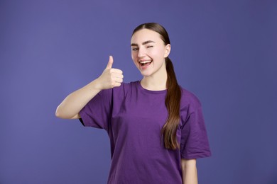 Photo of Happy woman showing thumbs up on purple background. Like gesture