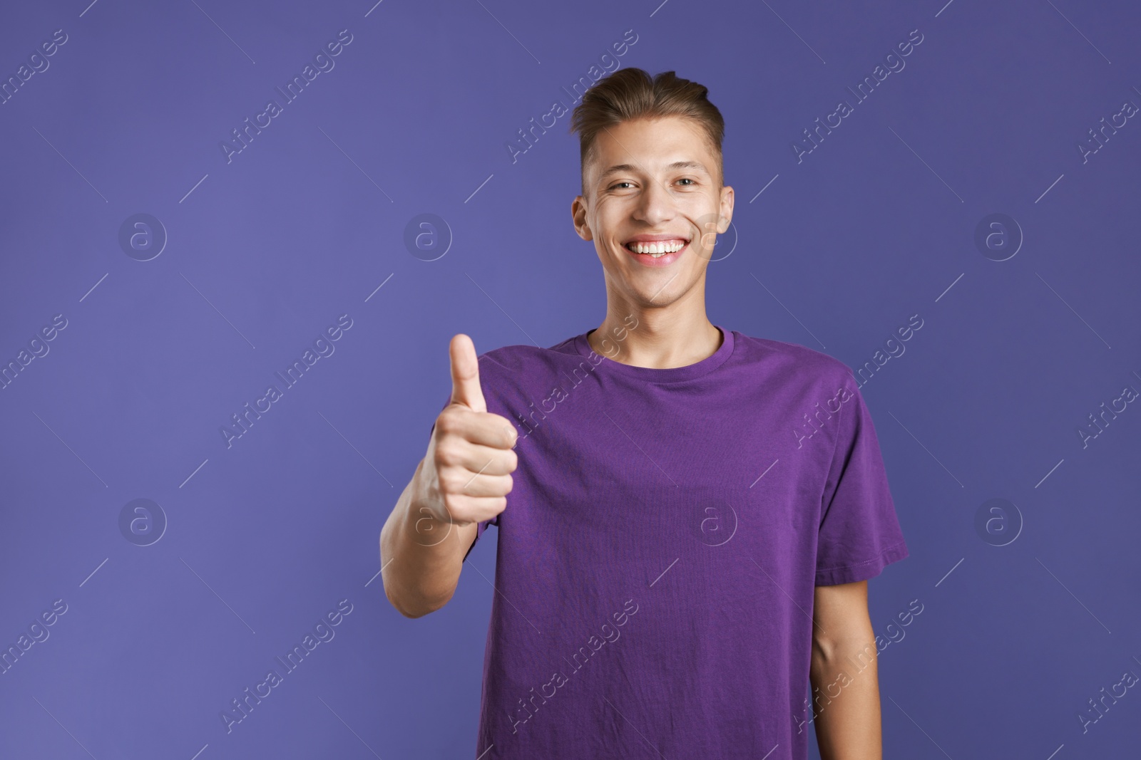 Photo of Happy man showing thumbs up on purple background, space for text. Like gesture