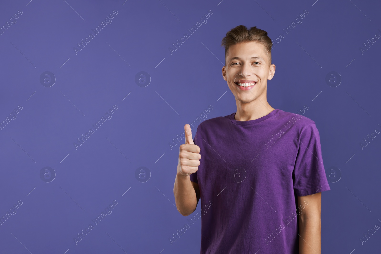 Photo of Happy man showing thumbs up on purple background, space for text. Like gesture