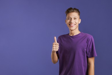 Photo of Happy man showing thumbs up on purple background, space for text. Like gesture