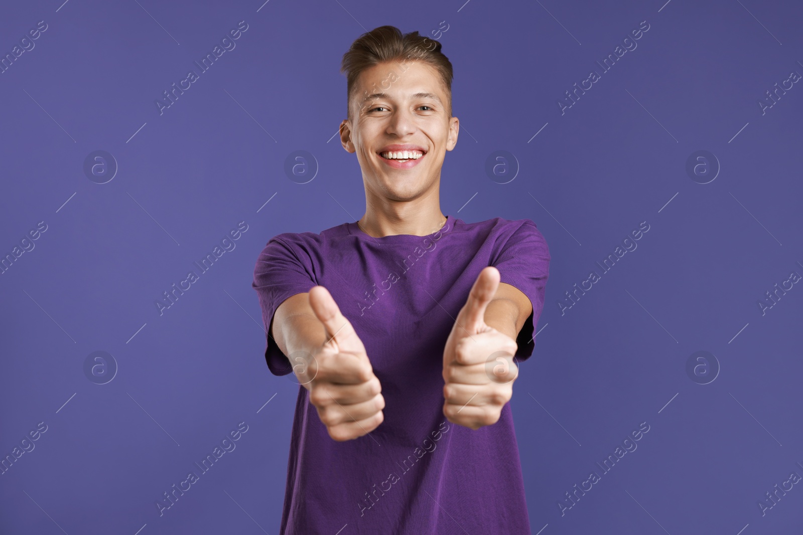 Photo of Happy man showing thumbs up on purple background. Like gesture