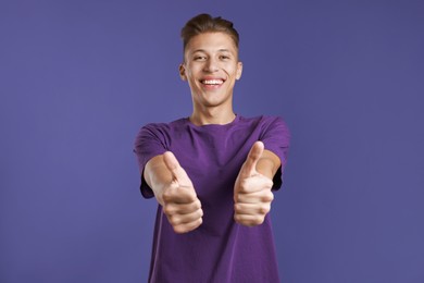 Photo of Happy man showing thumbs up on purple background. Like gesture