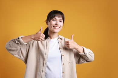 Photo of Happy woman showing thumbs up on orange background. Like gesture