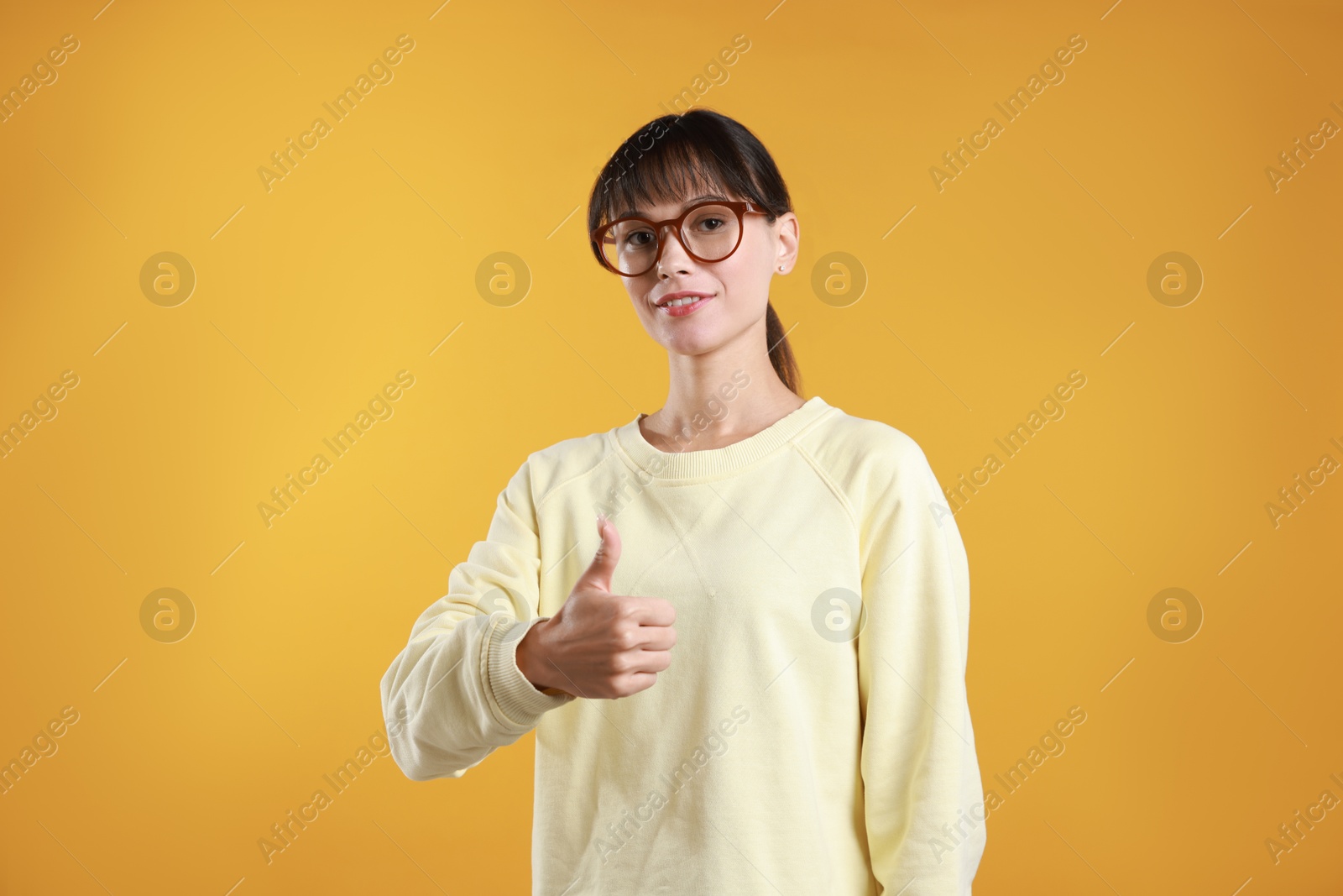 Photo of Happy woman showing thumbs up on orange background. Like gesture