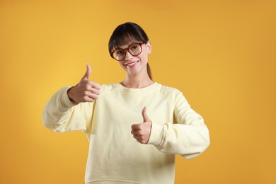 Happy woman showing thumbs up on orange background. Like gesture