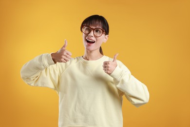 Photo of Happy woman showing thumbs up on orange background. Like gesture