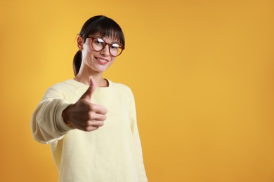 Photo of Happy woman showing thumbs up on orange background, space for text. Like gesture