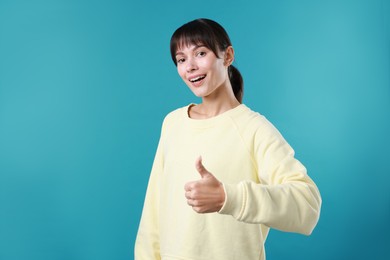 Photo of Happy woman showing thumbs up on light blue background, space for text. Like gesture