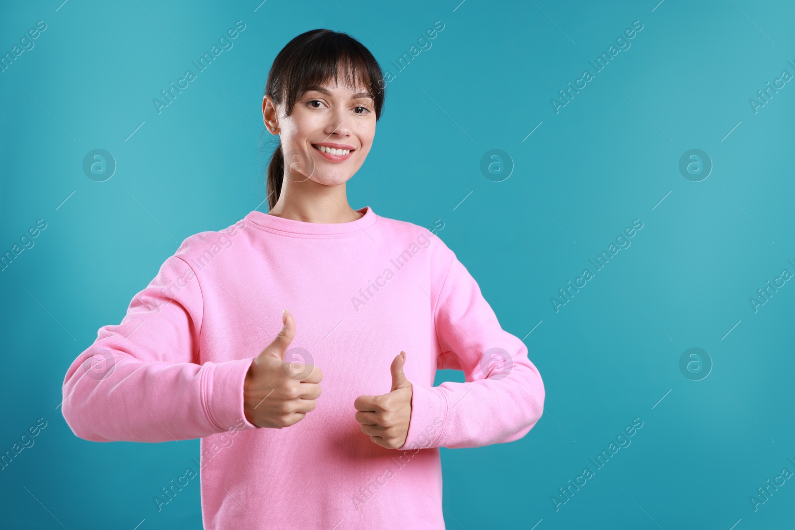 Photo of Happy woman showing thumbs up on light blue background, space for text. Like gesture