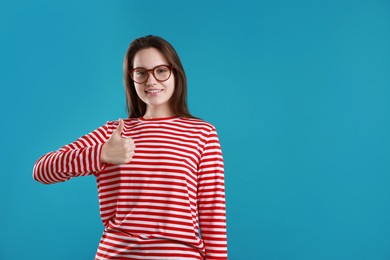 Photo of Happy woman showing thumbs up on light blue background, space for text. Like gesture