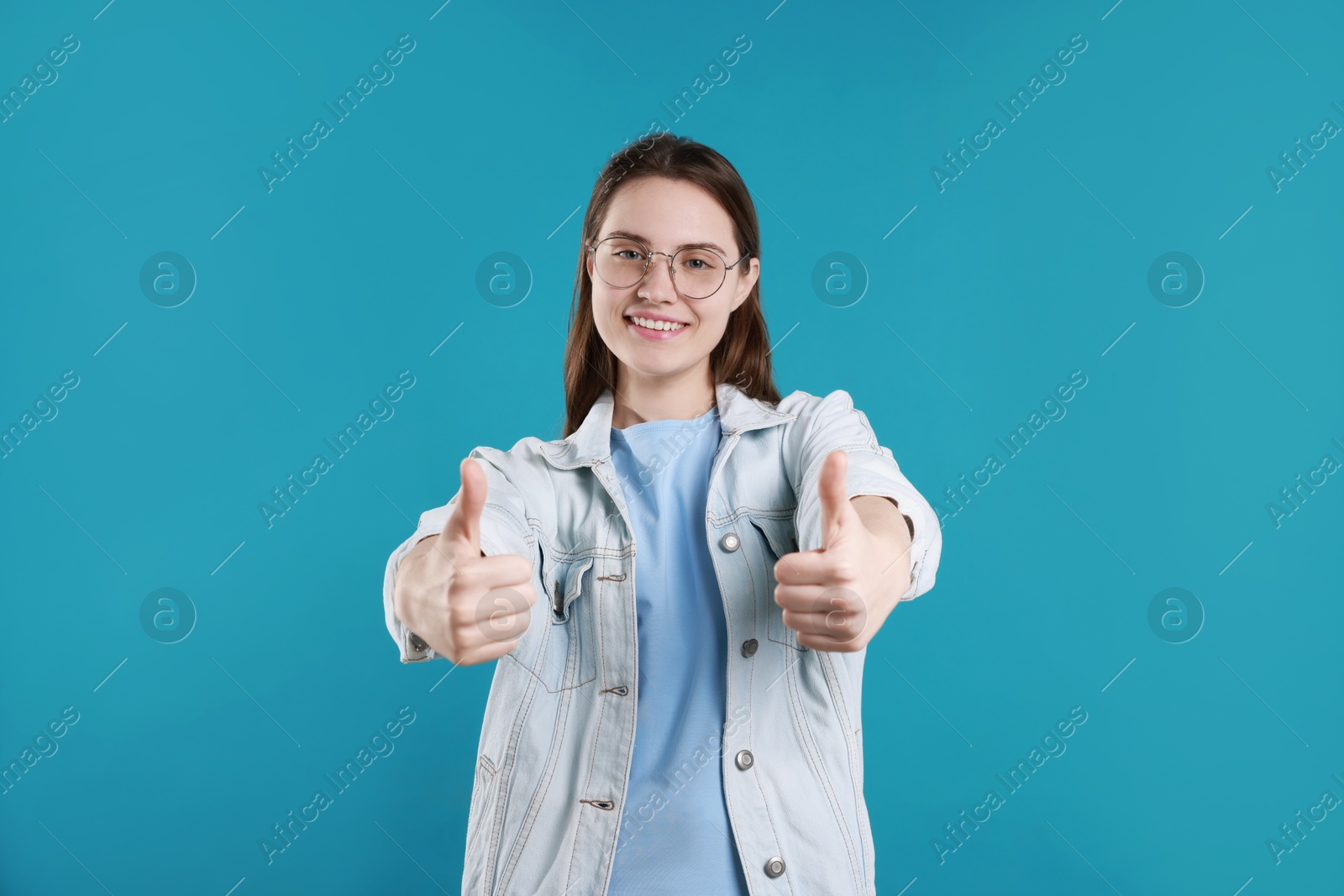 Photo of Happy woman showing thumbs up on light blue background. Like gesture