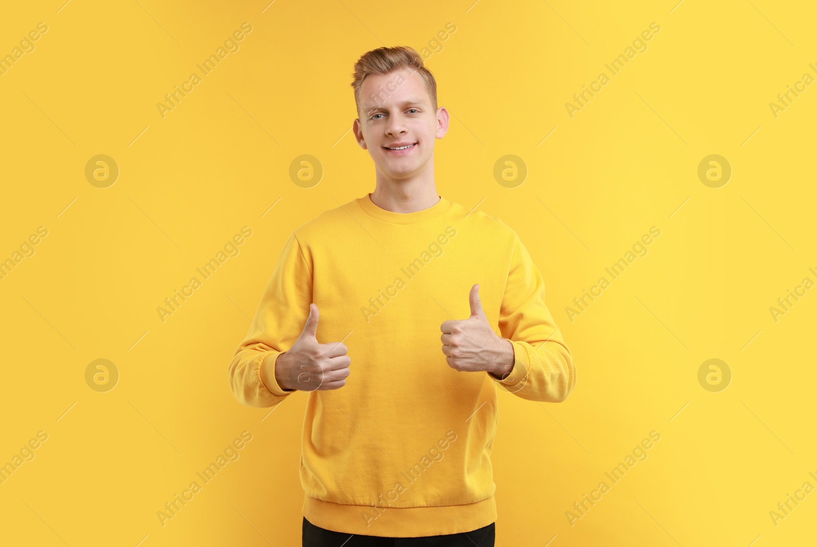 Photo of Happy man showing thumbs up on yellow background. Like gesture