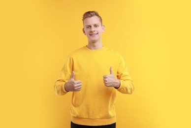 Photo of Happy man showing thumbs up on yellow background. Like gesture